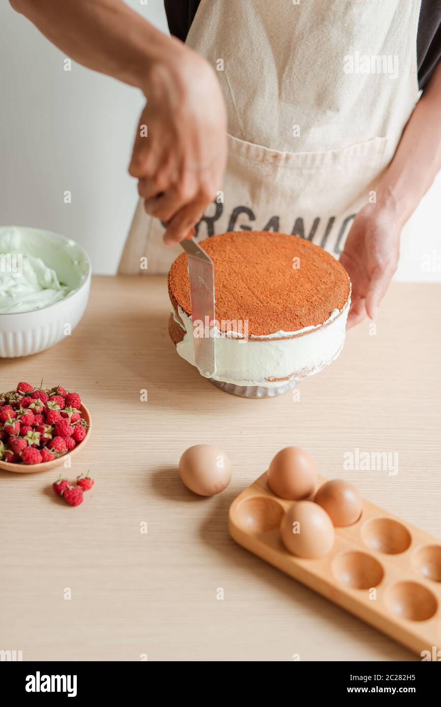 Man's hand levels cream on cake, cake decor. Making Sponge cake process. Stock Photo