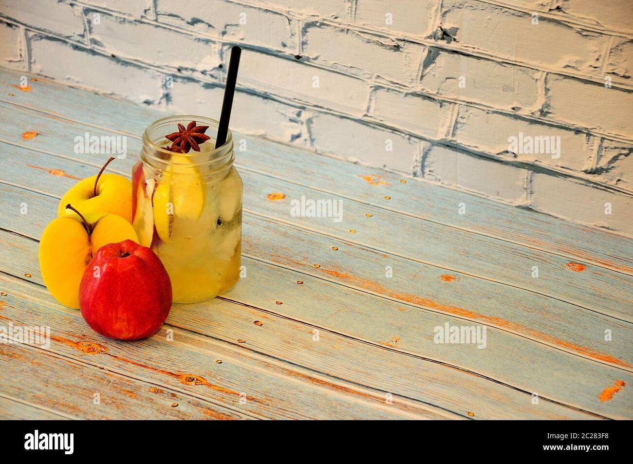 Red and yellow apples stand on a wooden table by the glass with juice and ice. Close-up. Stock Photo