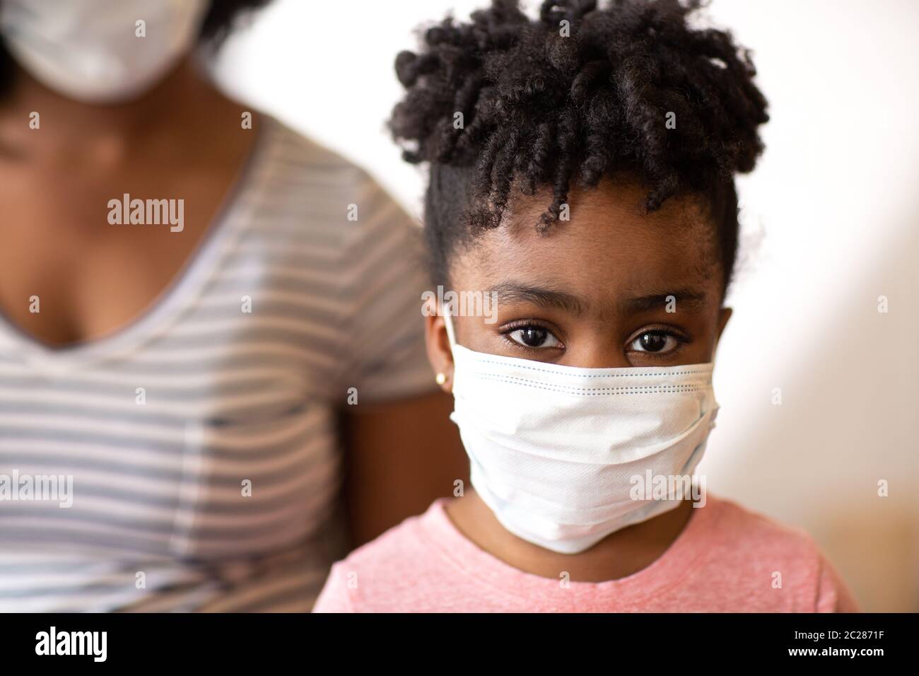 African American mother helping her daughter put on a face mask. Stock Photo