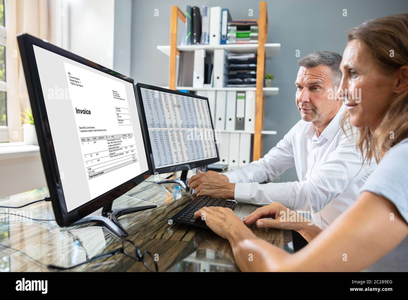 Side View Of Two Businesspeople Checking Invoice On Computer Over Desk