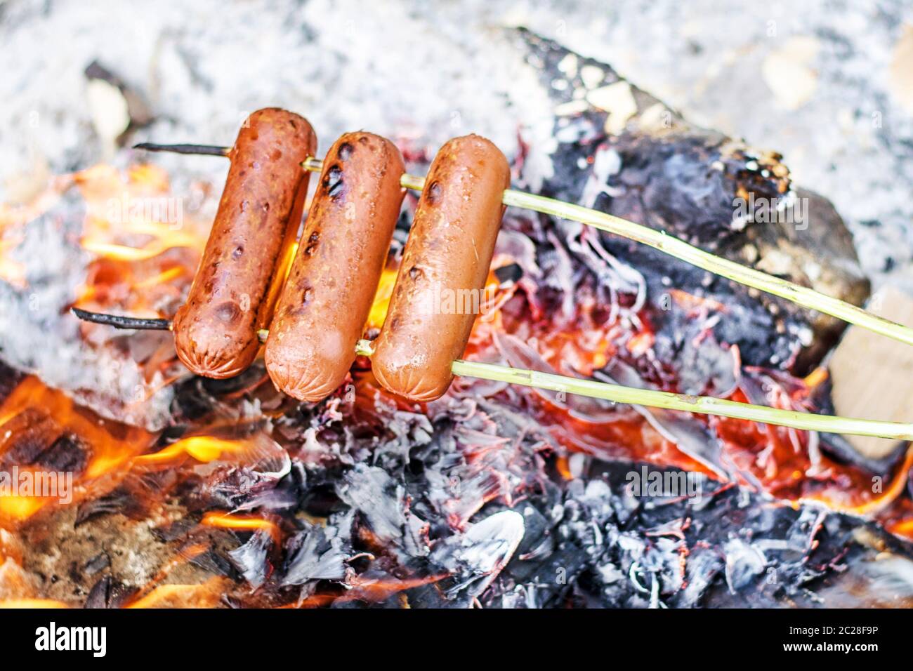 Grilling sausages over an open fire outdoors. Stock Photo
