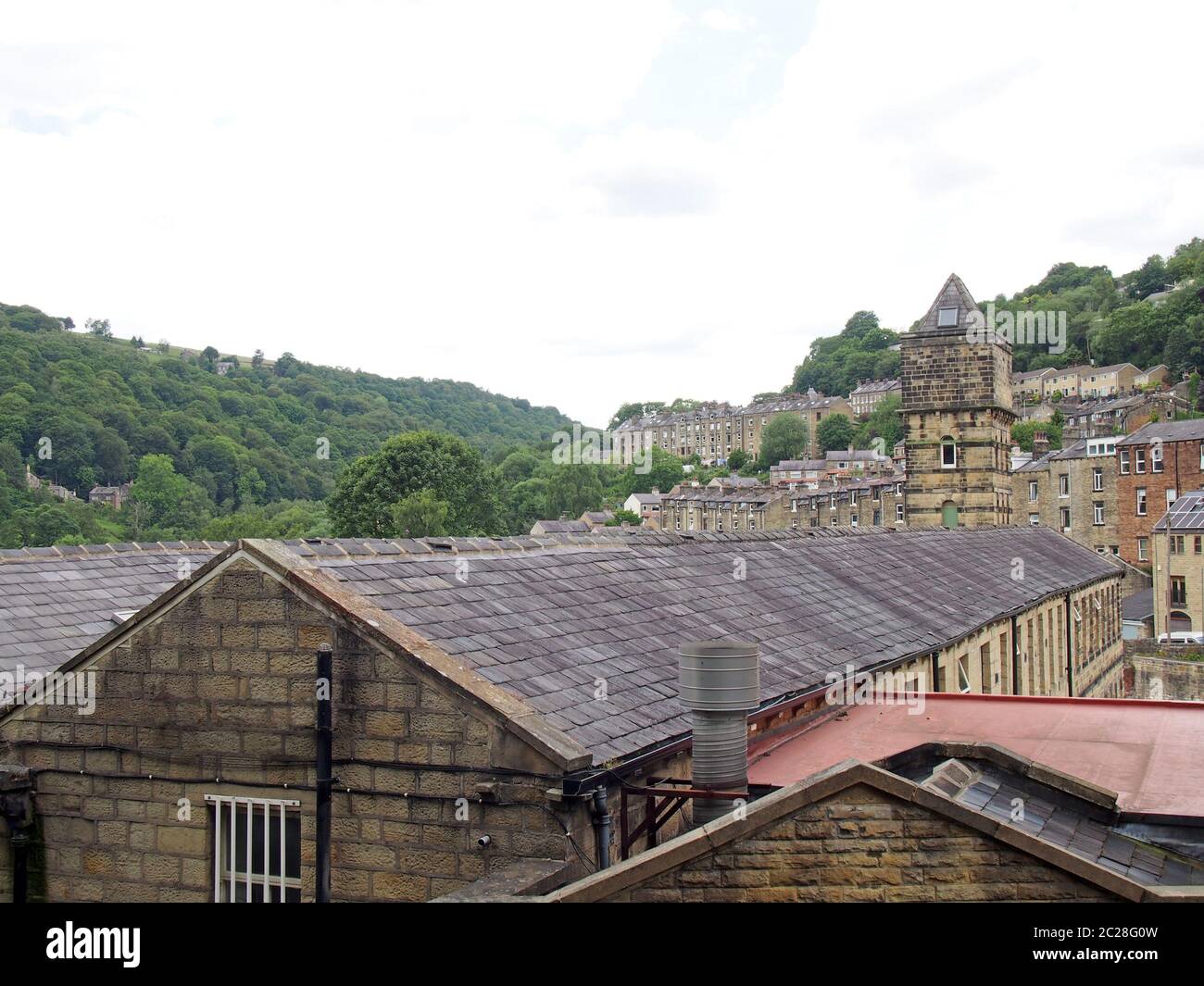 a view of the steep hillside streets in hebden bridge between summer trees with the tower of the historic nutclough mill buildin Stock Photo