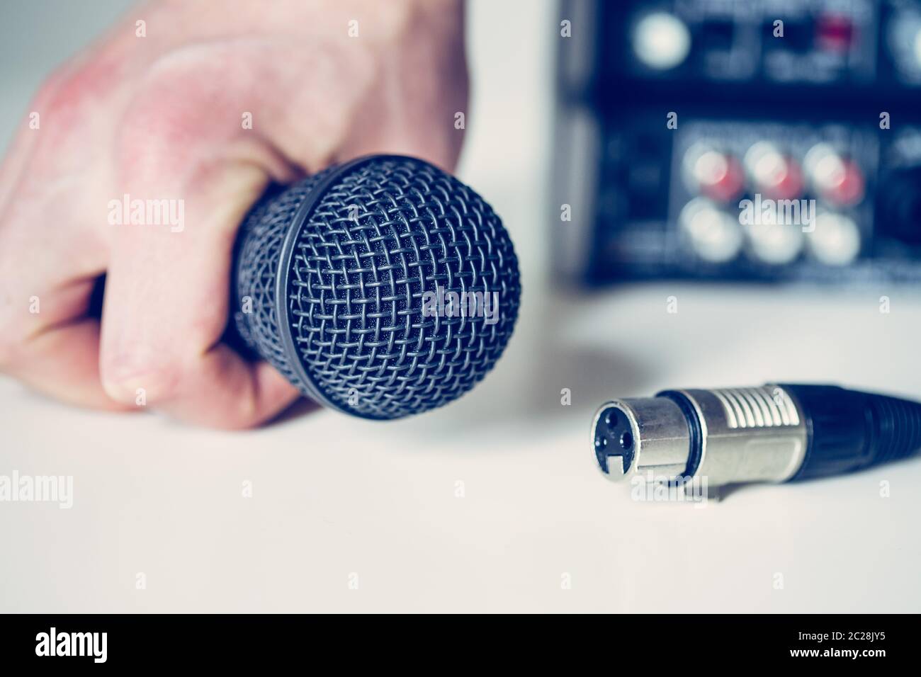 Black microphone holding in hand, and audio cable, mixer in the blurry background Stock Photo