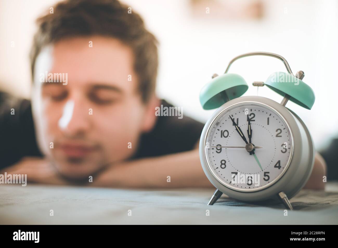 Alarm clock in the morning. Young man sleeps in the blurry background. Stock Photo