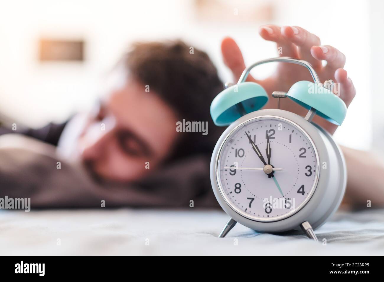 Alarm clock in the morning. Young wakes up in the blurry background. Stock Photo