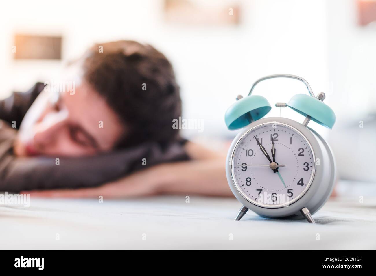 Alarm clock in the morning. Young man sleeps in the blurry background. Stock Photo