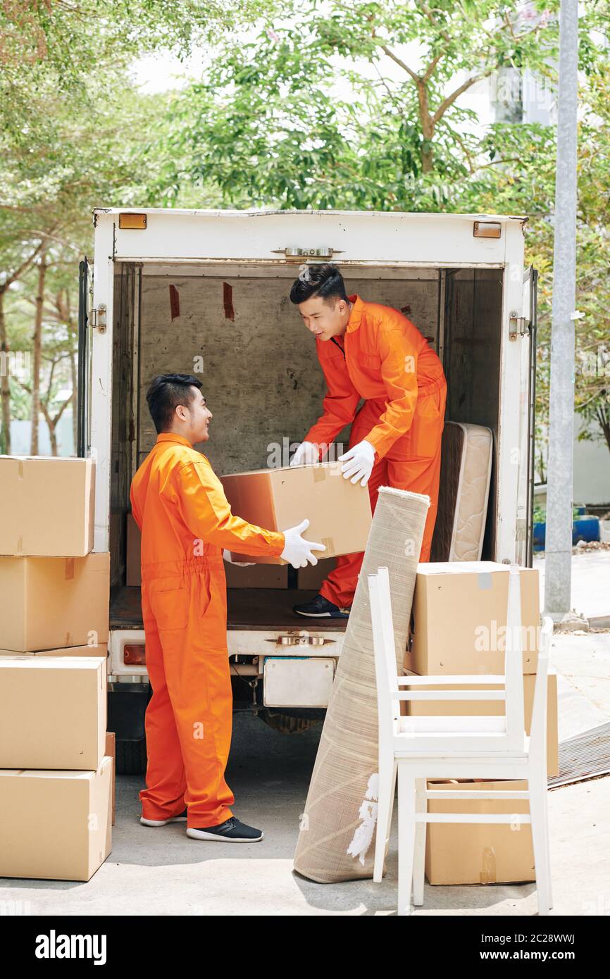 Two young adult men working in modern house moving service loading lorry with boxes, vertical