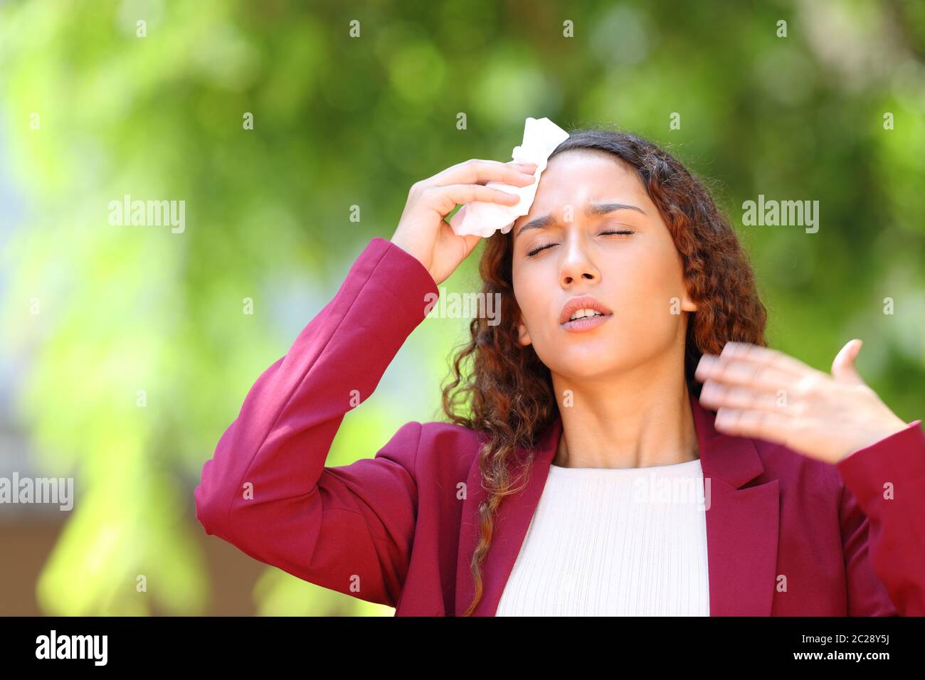 Stressed mixed race woman wearing jacket suffering heat stroke in a park Stock Photo