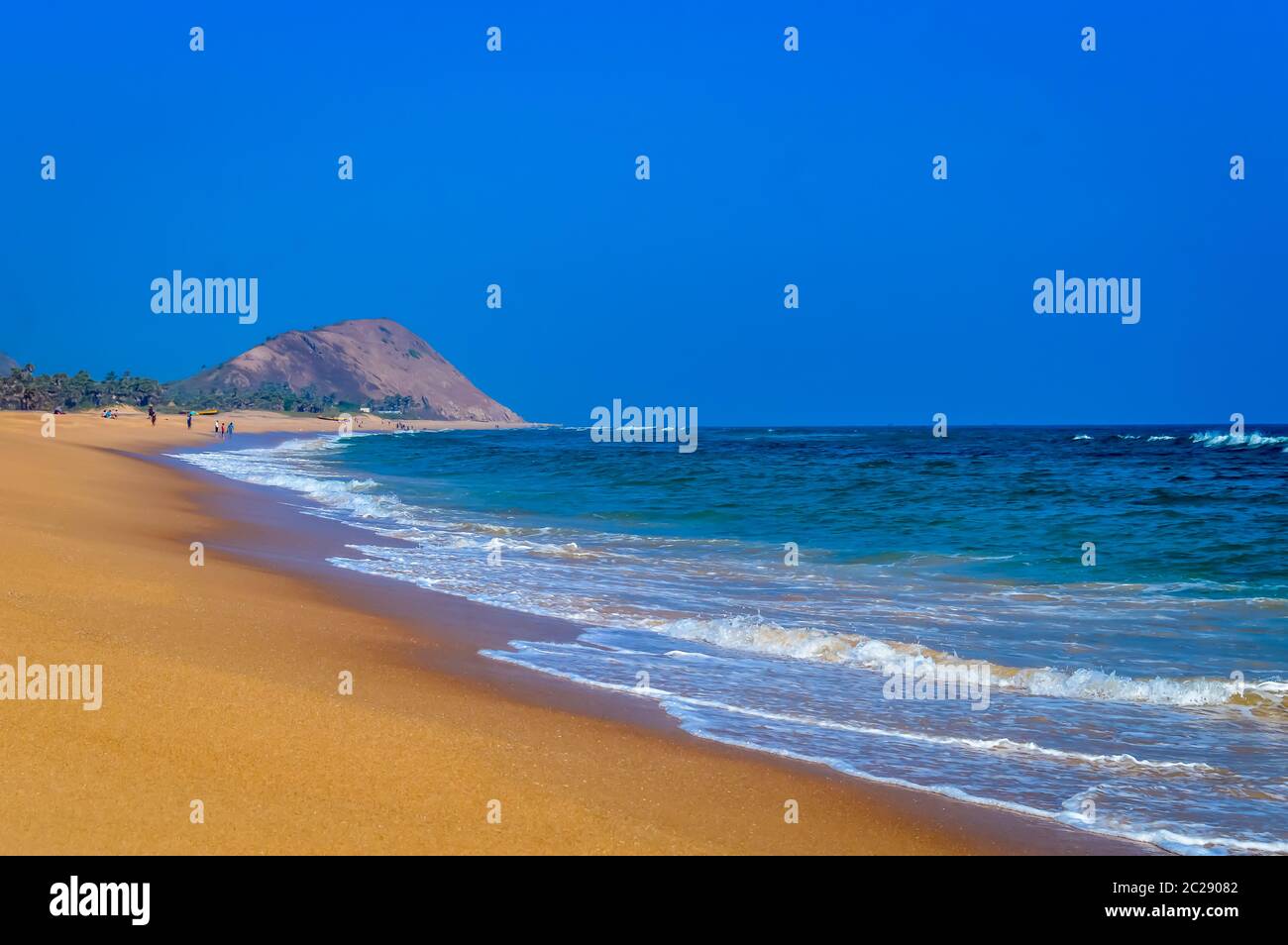 Wild Empty Tropical beach, vibrant yellow sand, bright blue sky, crystal clear waters with water crashing on the shore at daytime on a sunny day Stock Photo