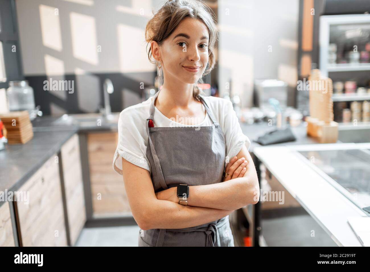 Portrait of a young and happy saleswoman at the counter in ice cream shop or cafe. Concept of a small business and retail Stock Photo