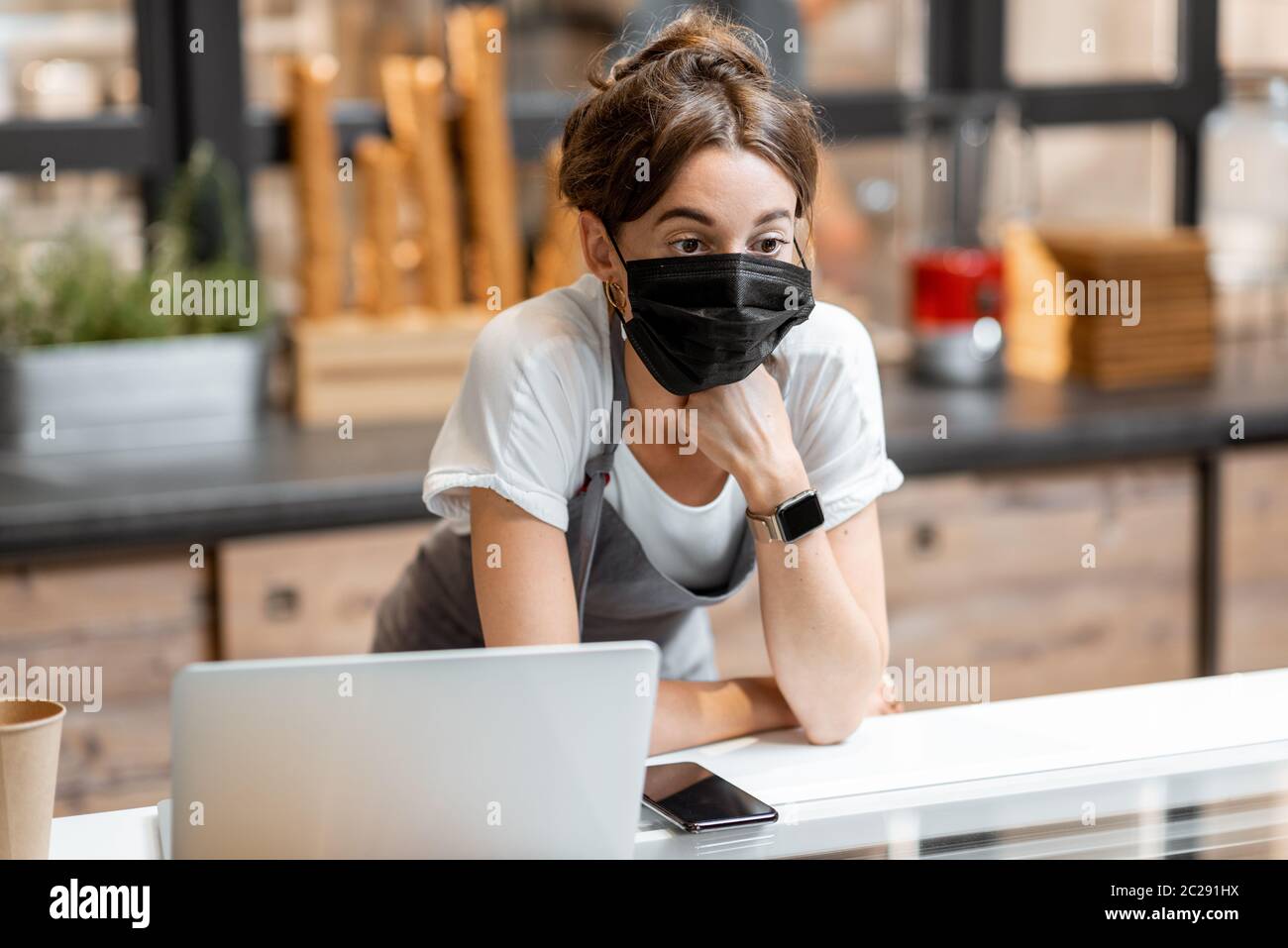 Portrait of a saleswoman or small business owner wearing medical mask at the counter in cafe or small shop. Concept of a retail business during a pandemic Stock Photo