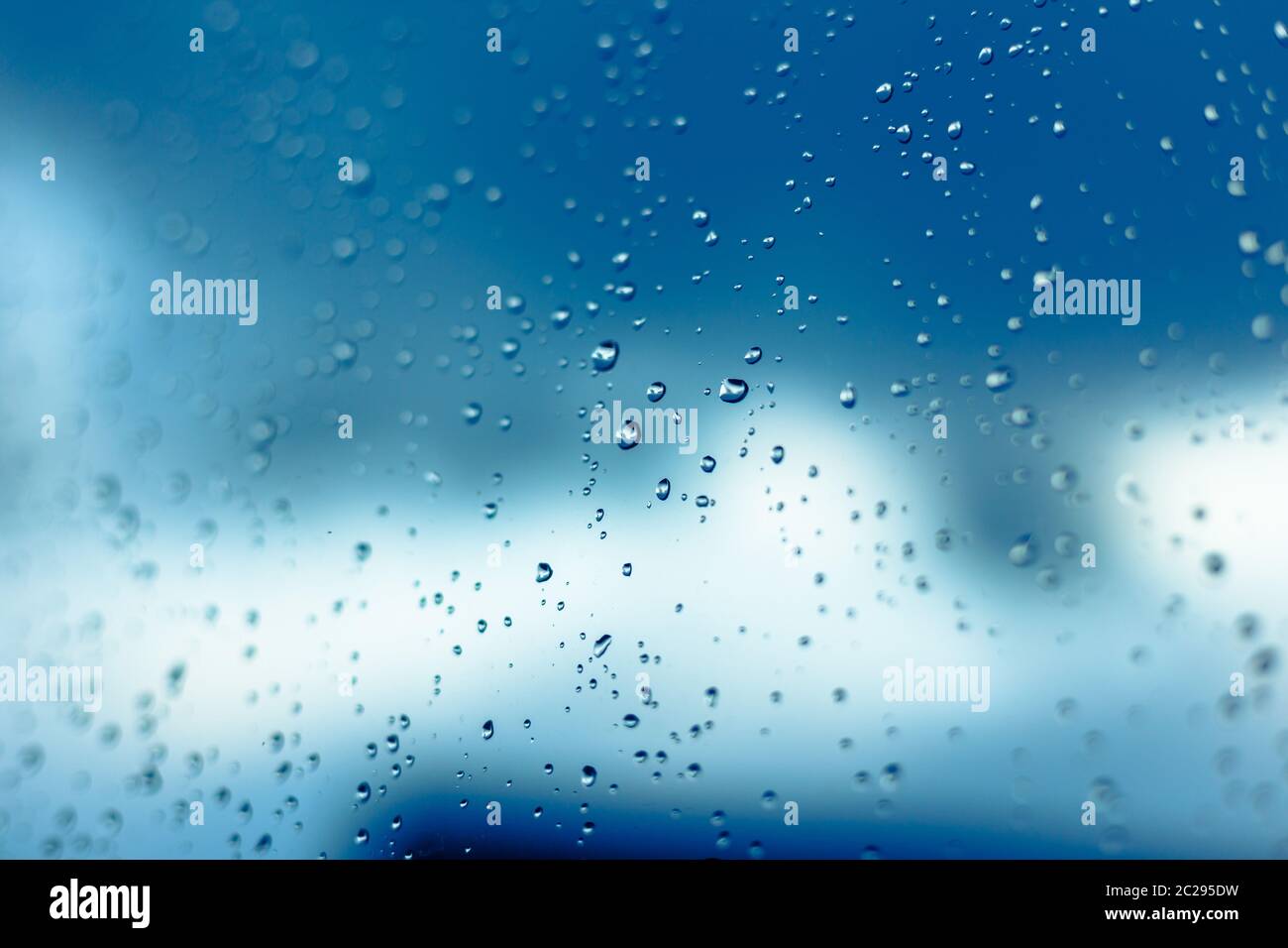 Water drops on the window, blue sky and clouds in the blurry background. Stock Photo