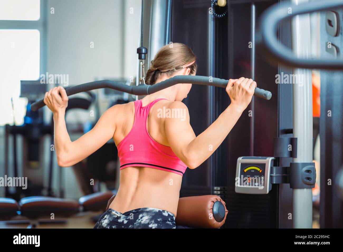 Rear view of a strong fit woman exercising lat pushdown behind the
