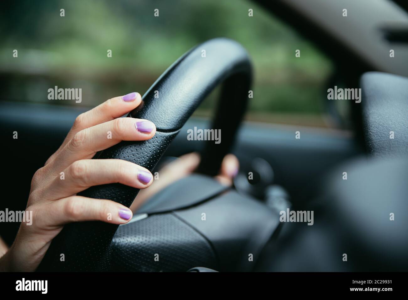 Sports car steering wheel, hands of a young girl with purple nail