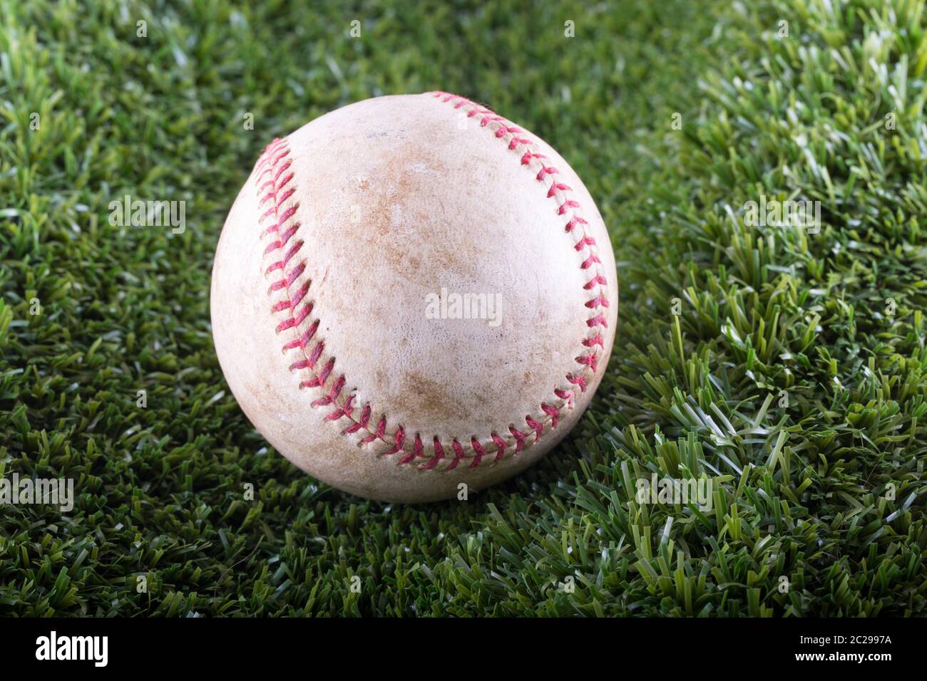 Old Baseball in closeup over synthetic grass, horizontal image Stock Photo