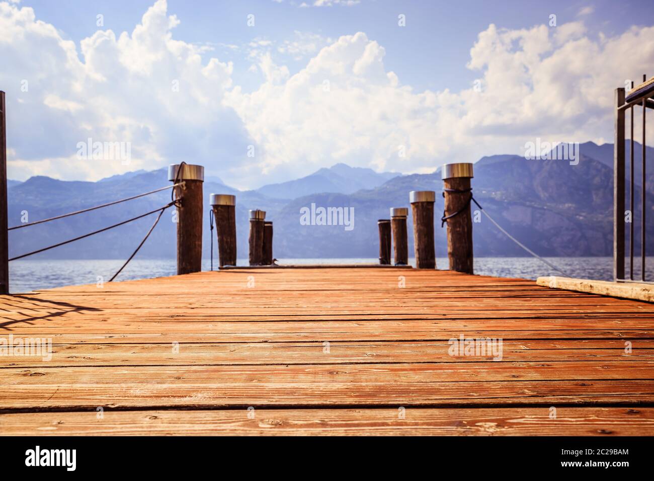 Wooden dock pier extending over blue lake water, mountains at lago di garda Stock Photo