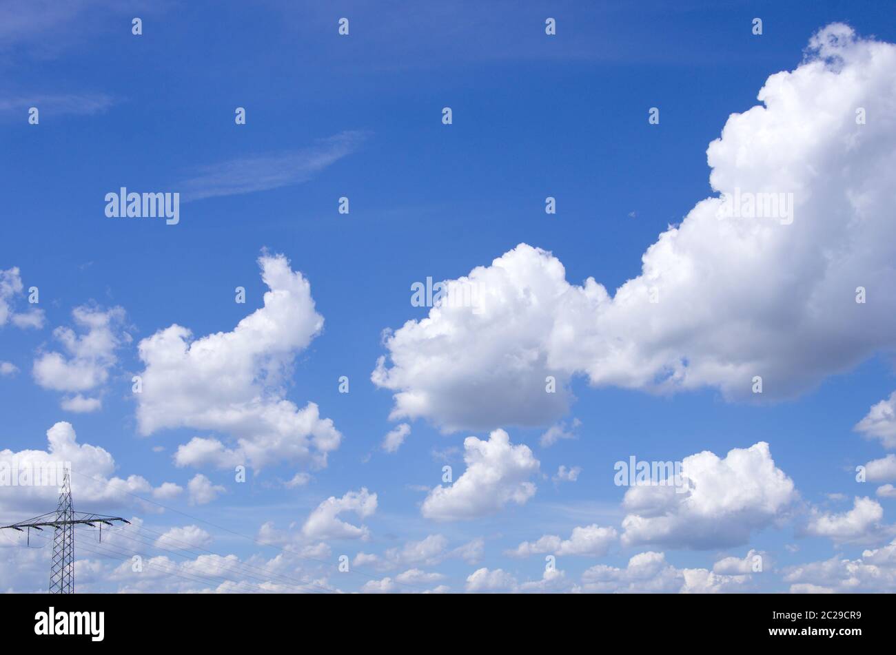 Panorama von flauschigen Schäfchenwolken vor blauem Himmel mit Stromleitung Stock Photo