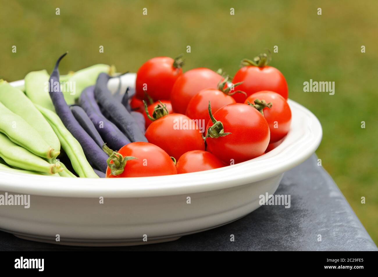 Calypso and French beans in a ceramic dish with ripe red tomatoes on a table outside Stock Photo