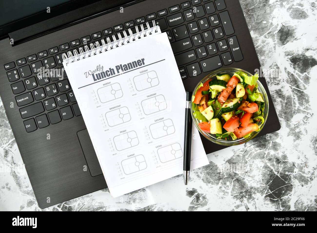 A meal plan for a week. Bowl with vegetable salad in the workplace near the computer. Lunch in the office during a break between work Stock Photo