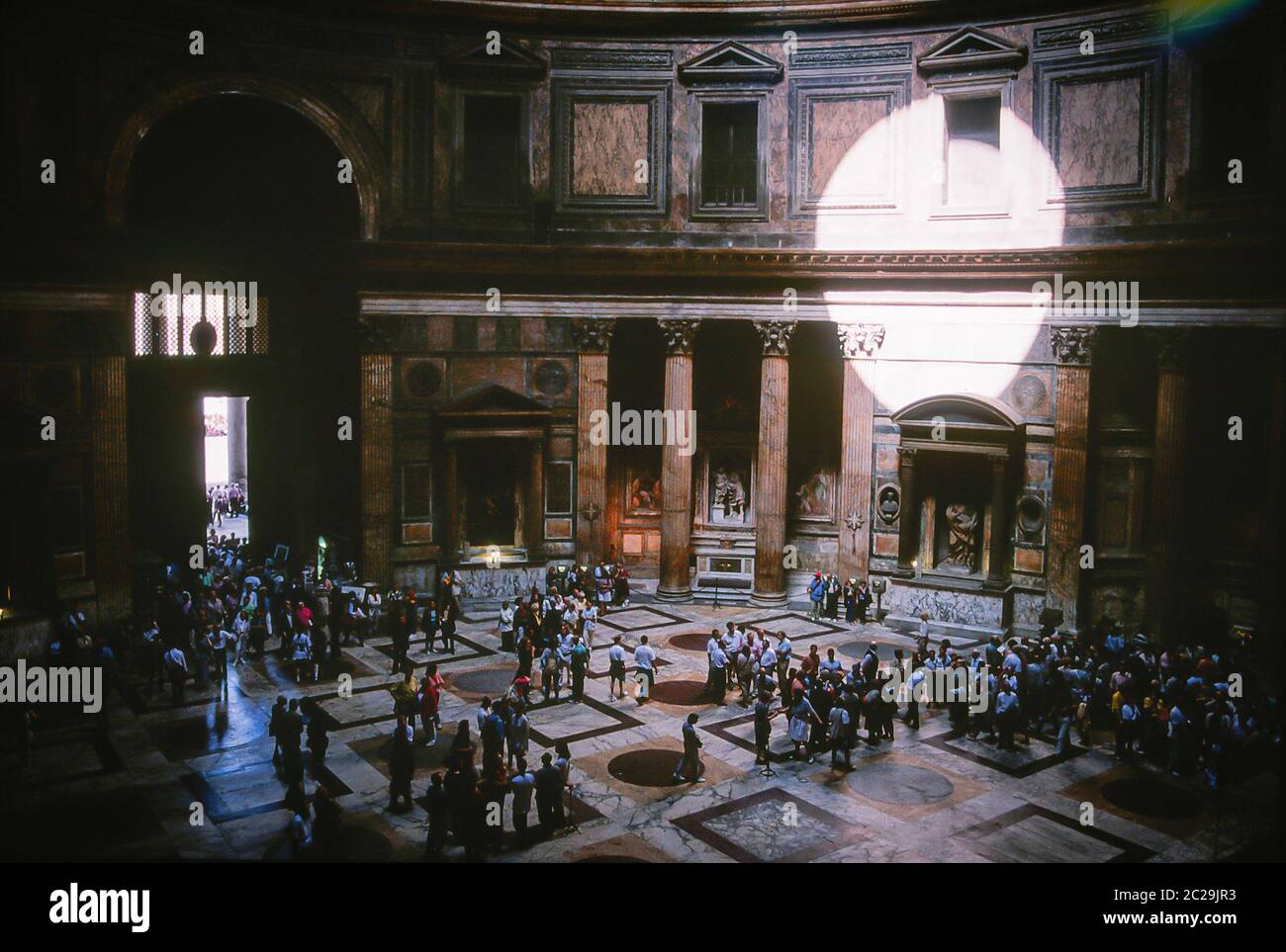 A different unusual view inside the iPantheon Rome looking down on tourists from the 1st floor balcony and the sun disc shining on the wall, Stock Photo