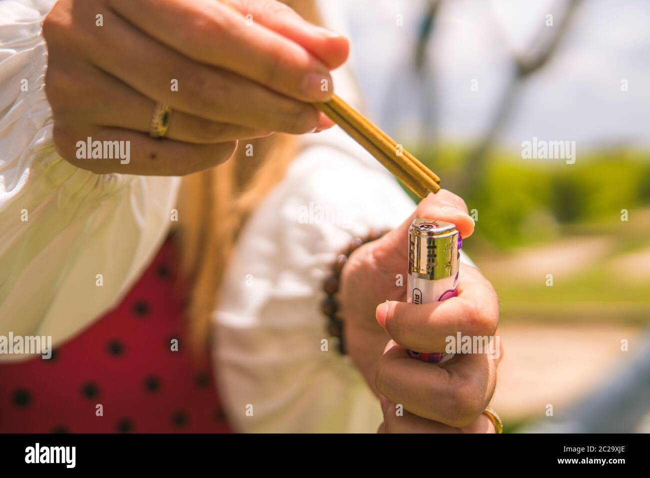 Closeup of a woman's hand burning incense. The background is an