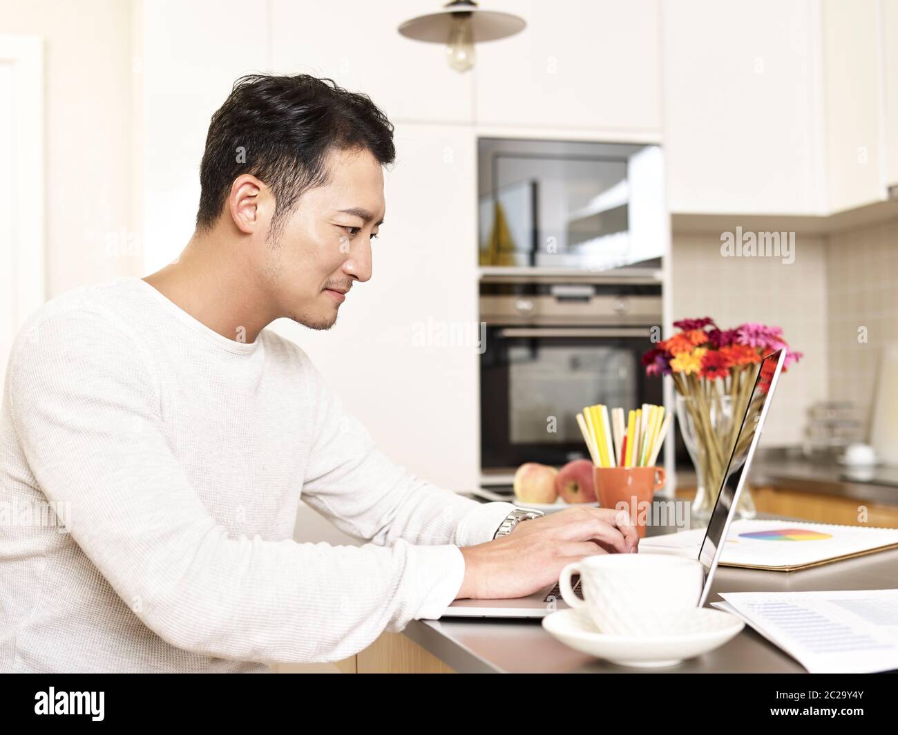young asian businessman working from home sitting at kitchen counter using laptop computer Stock Photo