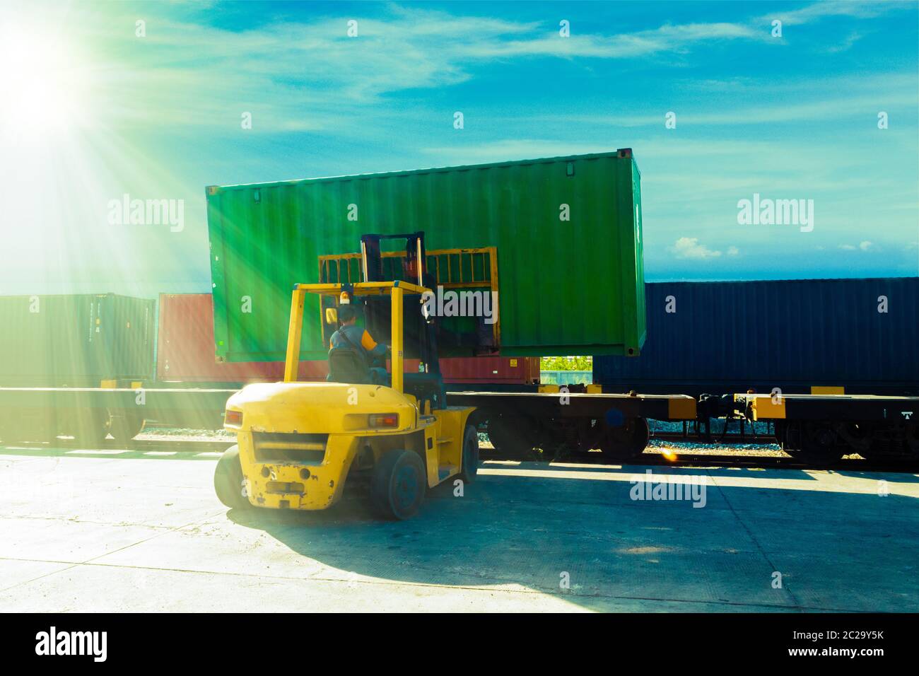 Forklift lift on empty container onto freight train inside rail yard. Rail road logistics operations. Stock Photo