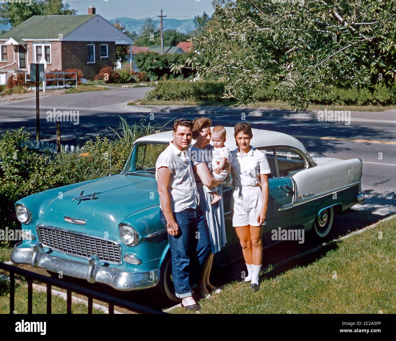 A family posing next to their two-tone Chevrolet Bel Air parked in their suburban driveway, USA, 1961. The group includes the young couple's baby. This Chevy, a 2-door hardtop, was made from 1953 to 1957. Stock Photo