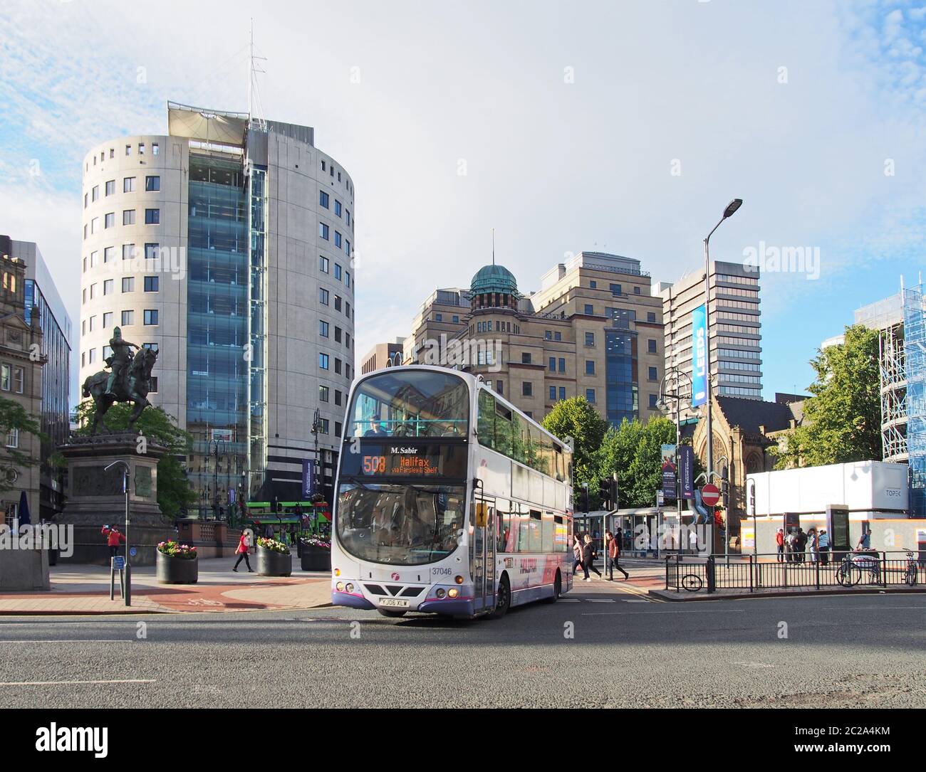 a bus in city square in leeds west yorkshire with people walking past city buildings and monuments in bright summer sunshine Stock Photo