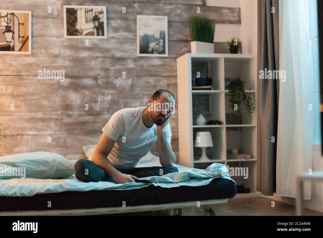 Sleepy man watching tv sitting on comfortable bed Stock Photo Alamy