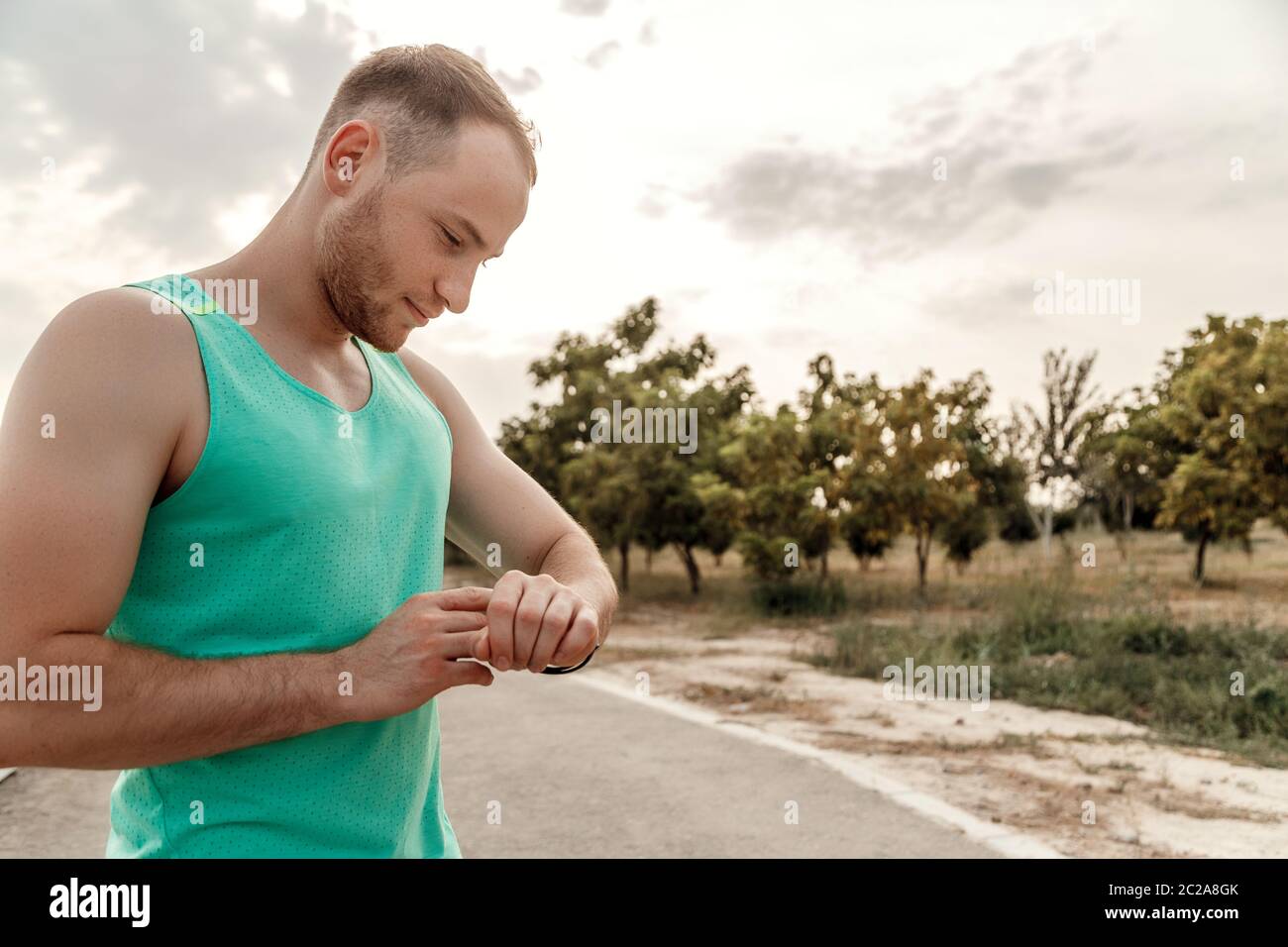 portrait of Caucasian guy in azure t-shirt looking at fitness tracker readings after or before Jogging. Stock Photo