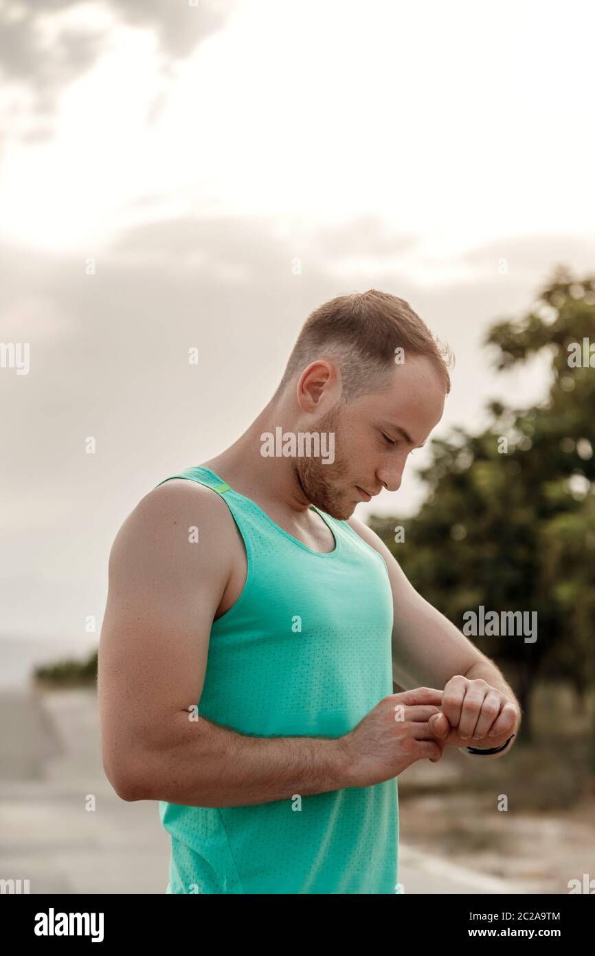 portrait of Caucasian guy in azure t-shirt looking at fitness tracker readings after or before Jogging. Stock Photo