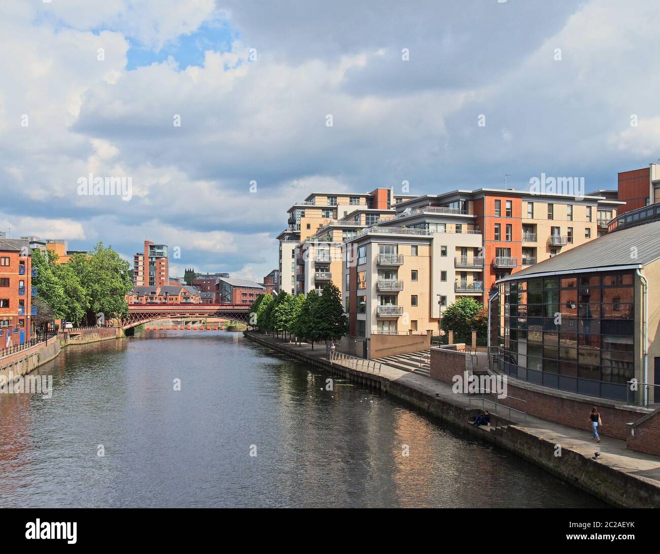 a view of the river aire in leeds with apartment buildings around crown point bridge and people walking along the waterfront Stock Photo