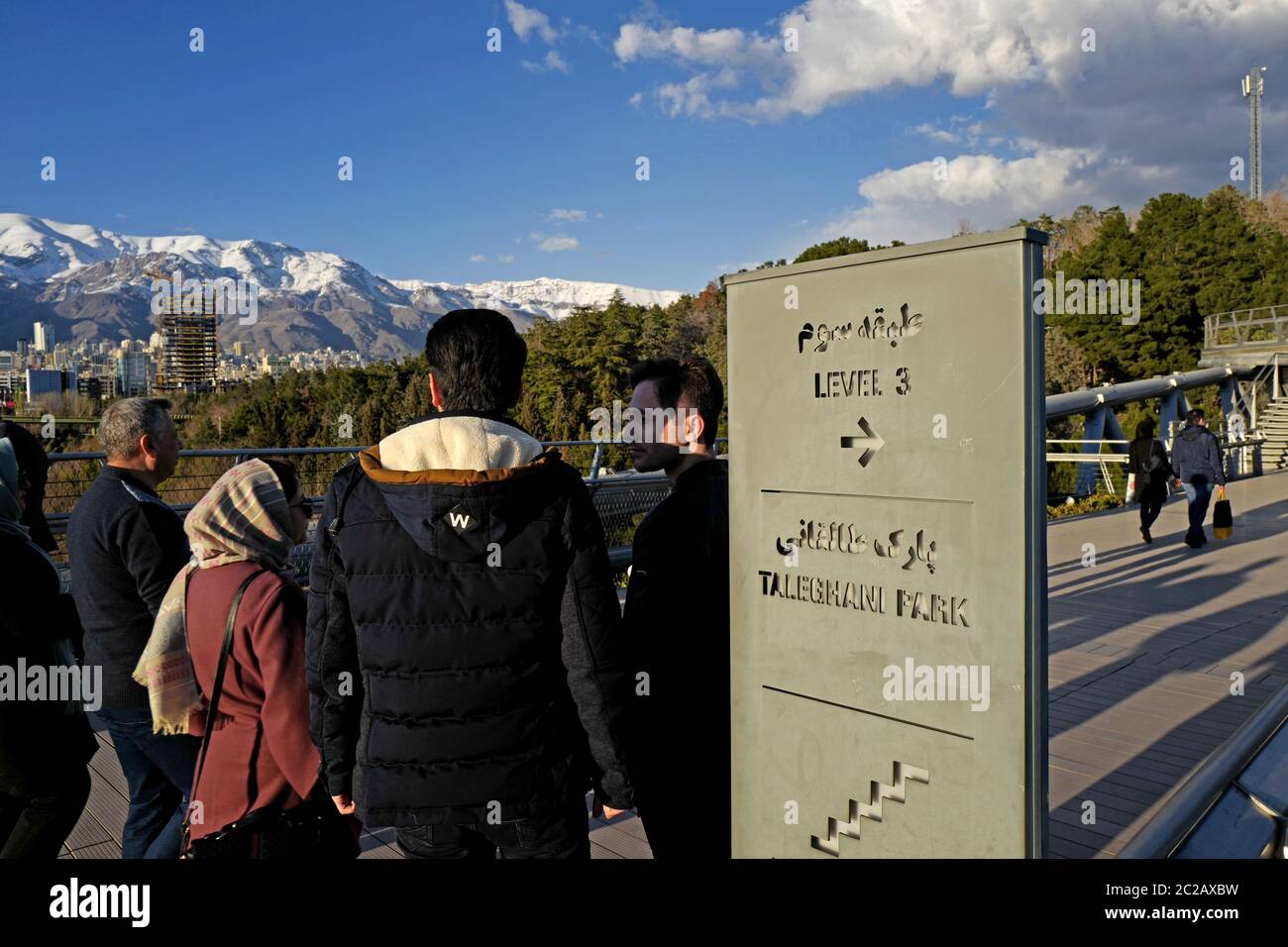 Iranian people crossing the modern Tabiat pedestrian bridge, to Taleghani Park, with the Alborz snow mountains in the background, in Teheran. Stock Photo