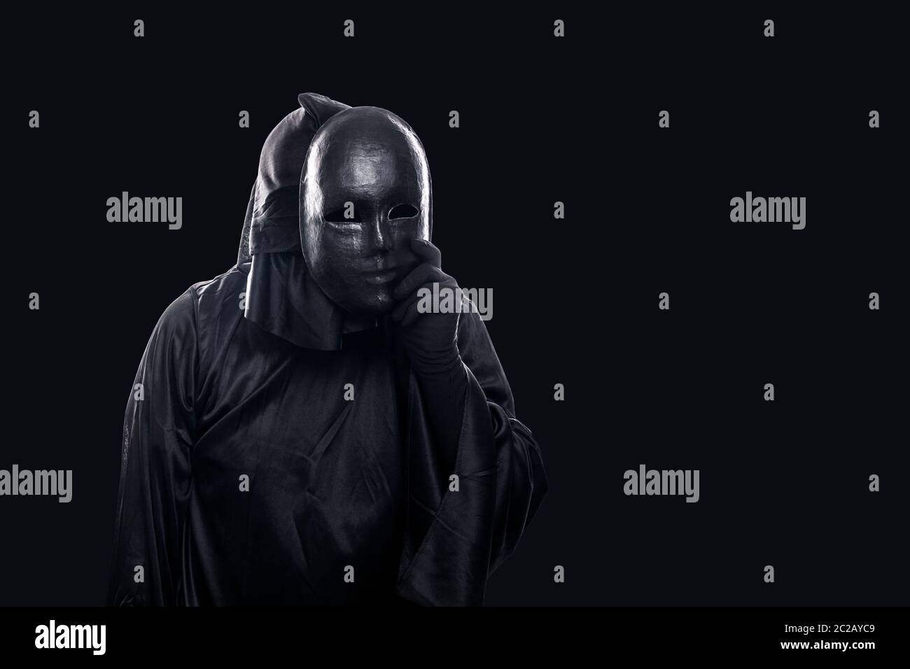 Scary figure in hooded cloak with mask in hand isolated on black background Stock Photo