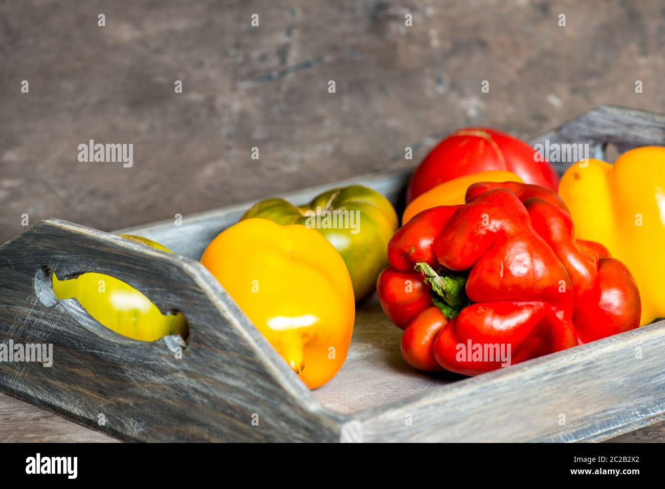 Imperfect natural peppers and tomatoes on an old wooden tray on a dark background. Copy Space. Stock Photo