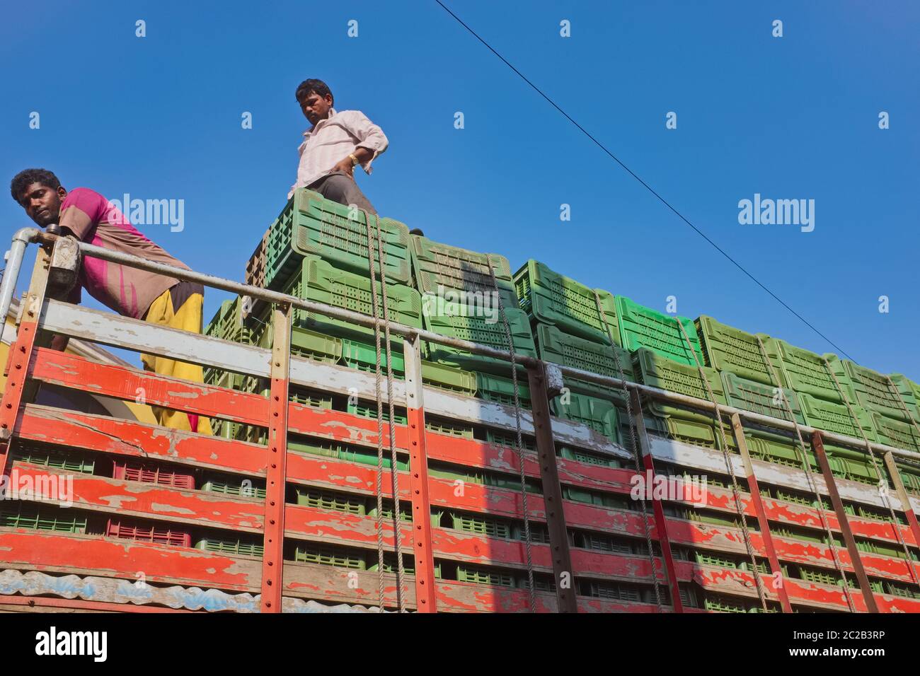 Employees of a trucking company standing on top of a truck laden with goods, against a deep blue, sunny sky; Mumbai, India Stock Photo