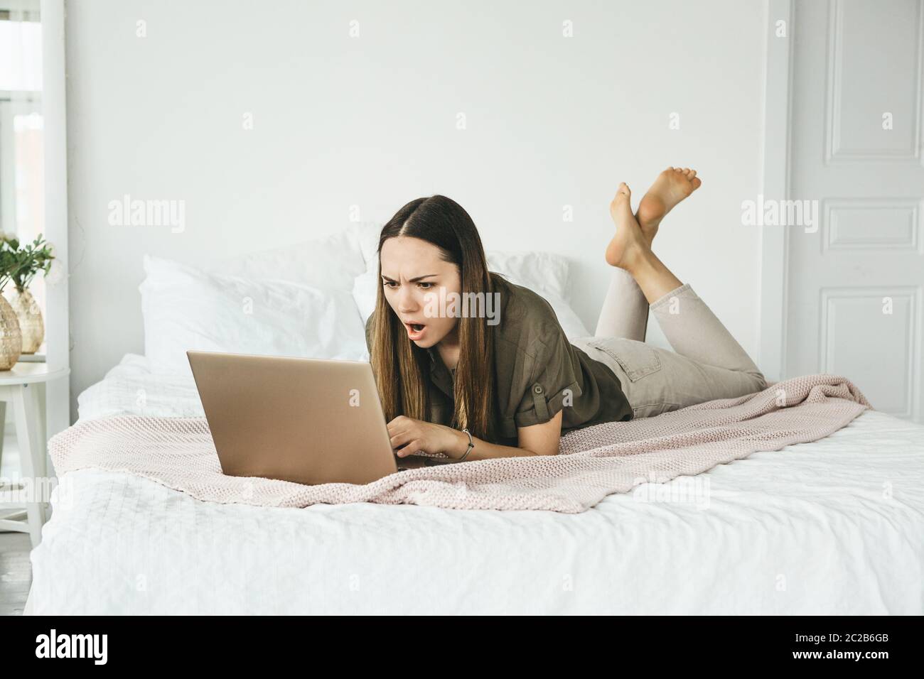 The girl uses a laptop at home. She saw information or news and was unpleasantly surprised or angry or upset. Stock Photo