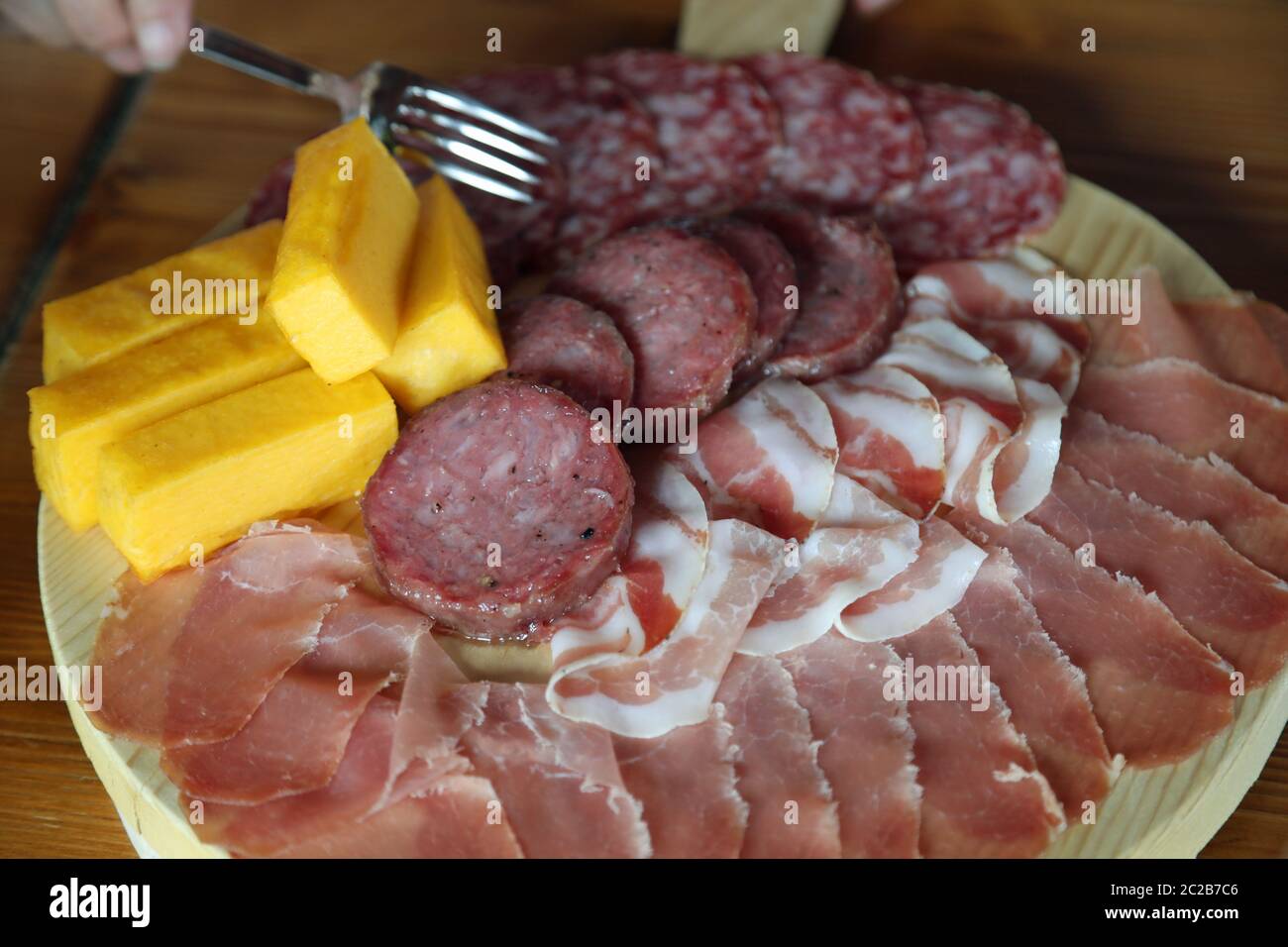 fork that takes mixed cold cuts from the wooden cutting board in the Italian farmhouse Stock Photo