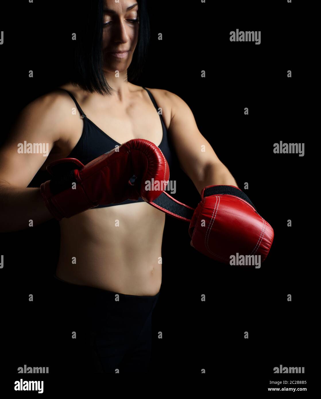 beautiful young girl of athletic appearance with black hair dresses red leather boxing gloves, low key Stock Photo