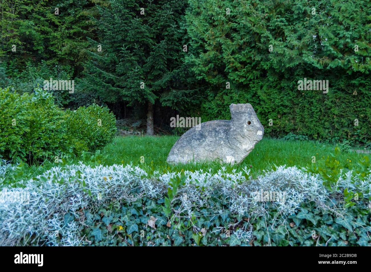 Sculpture of a stone rabbit on a lawn next to a bush in the city of Meix in front of Virton in Belgium Stock Photo