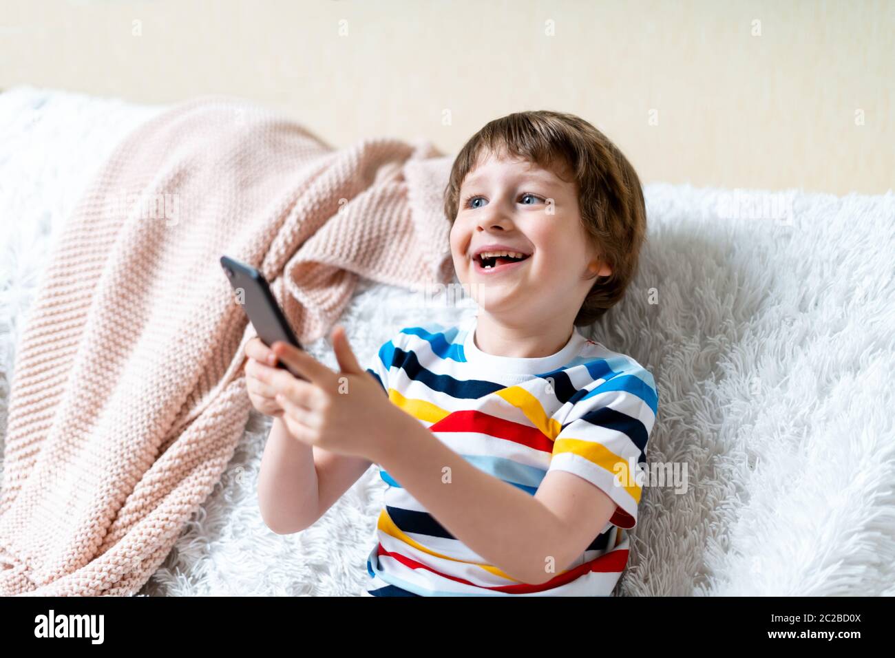 Happy little child boy playing online game, watching video on cellphone,  sitting on couch entertaining in living room. Smiling small kid using funny  m Stock Photo - Alamy