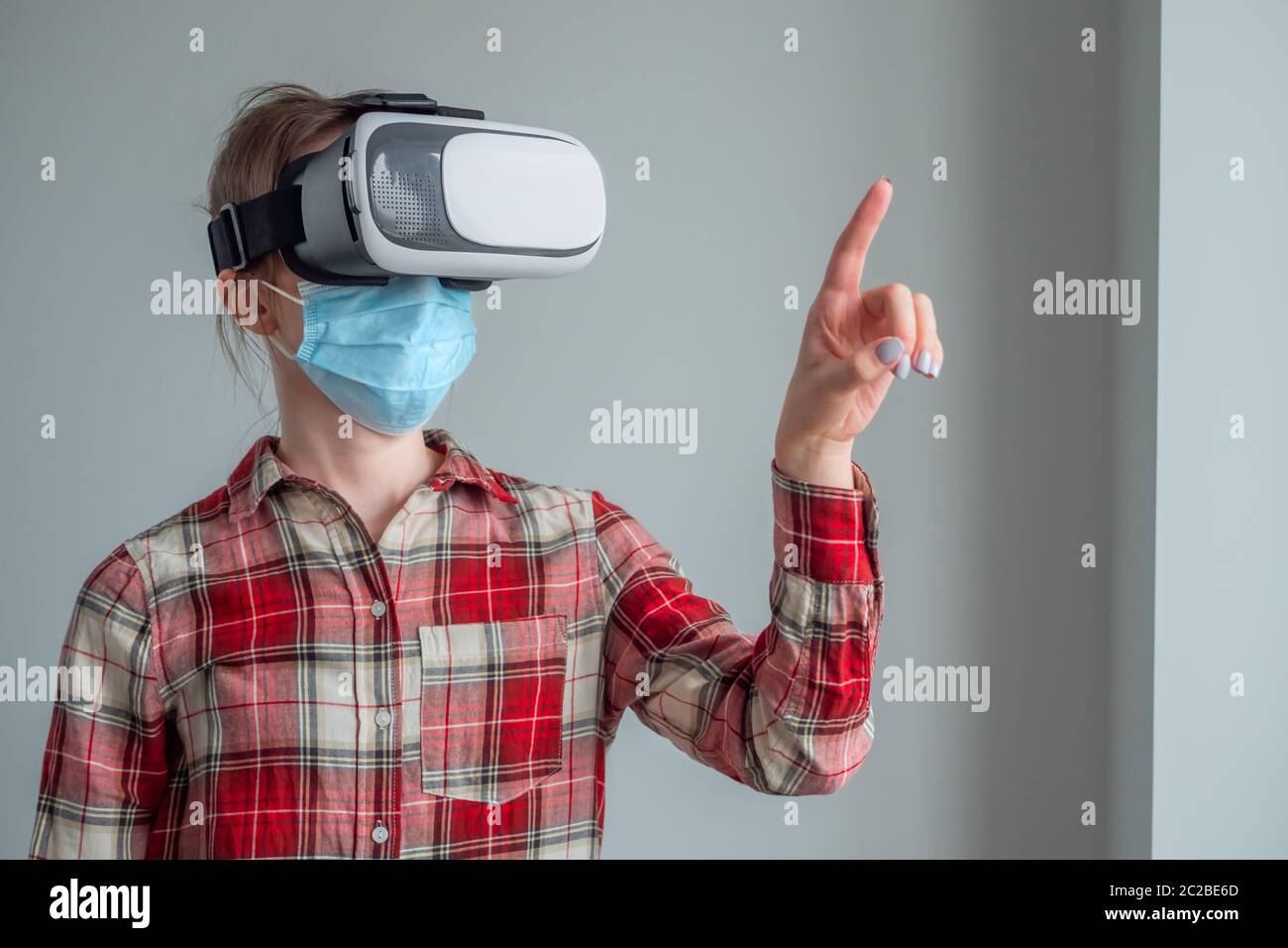 Portrait of woman wearing medical face mask, red plaid shirt, virtual  reality headset and moving hand at home. VR, self isolation, prevention  Stock Photo - Alamy