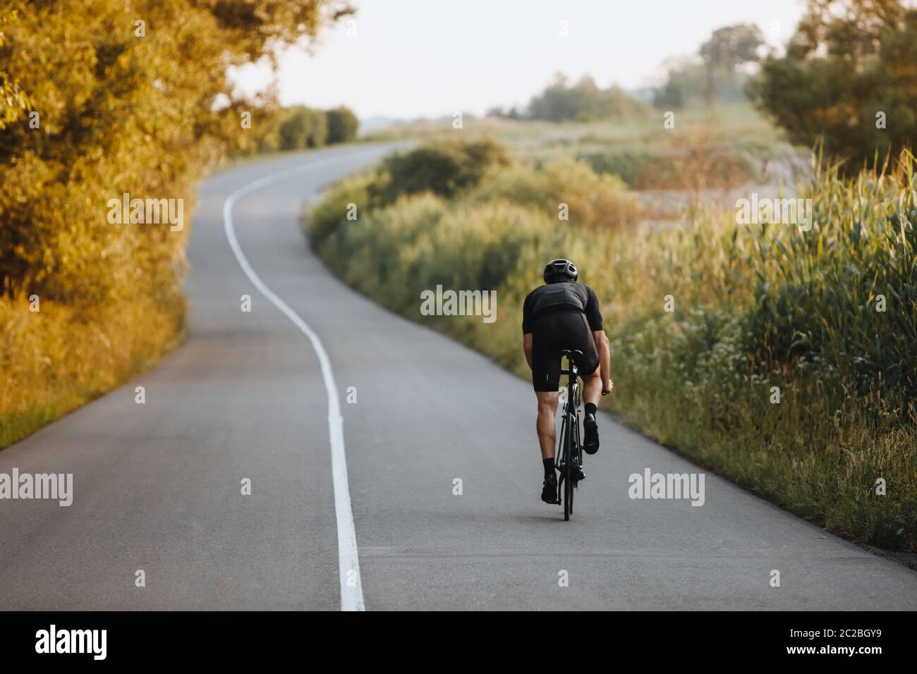 Back view of strong male cyclist with athletic body shape riding bike at  the paved road among trees and green bushes in black protective helmet and  sp Stock Photo - Alamy