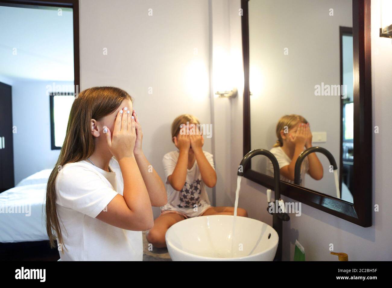 Happy children girls are washing their faces in a bathroom Stock Photo