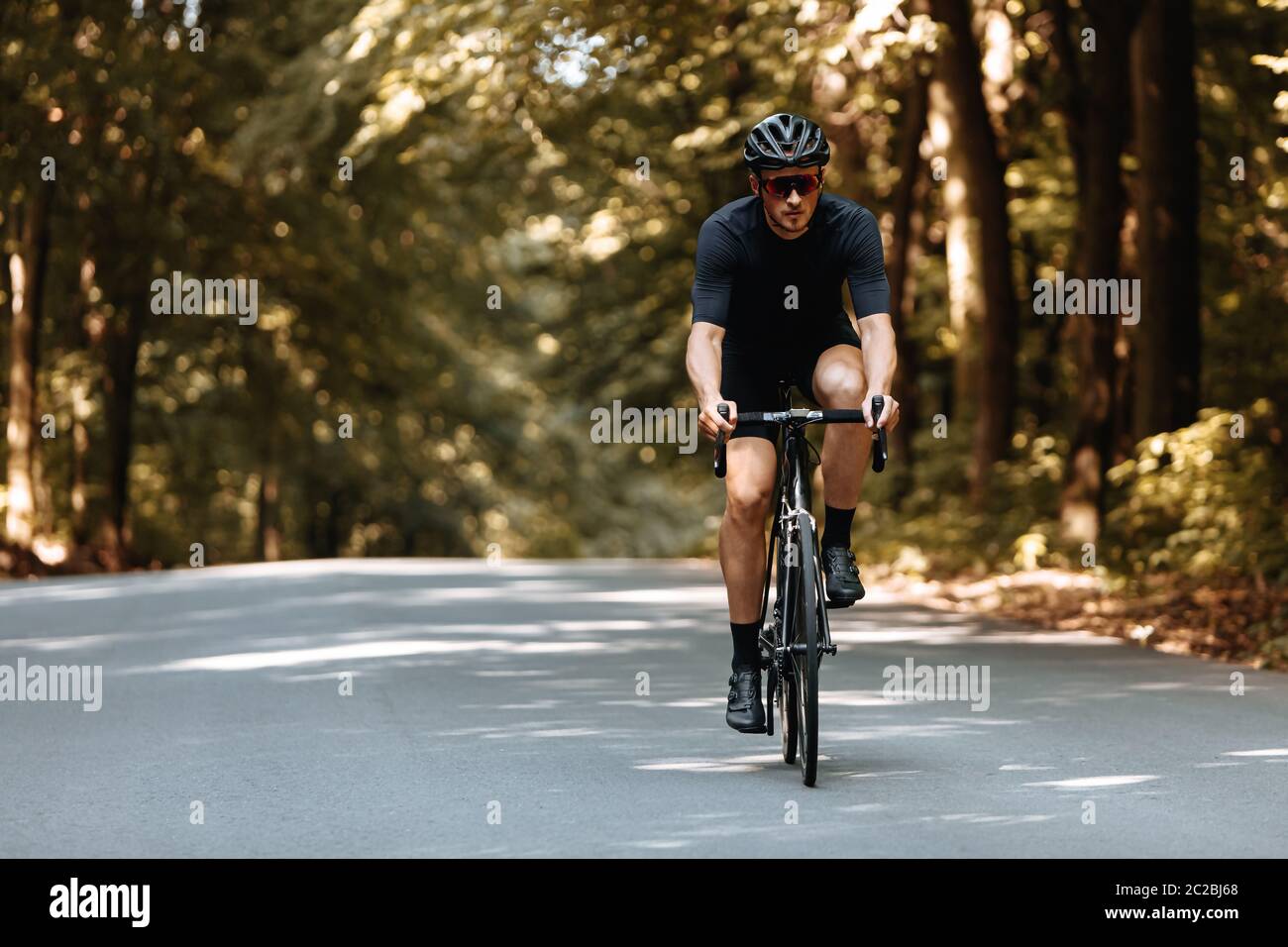 Mature bearded man in active wear and protective helmet dynamically riding bike on paved road. Bicyclist in mirrored eyeglasses enjoying favore hobby Stock Photo