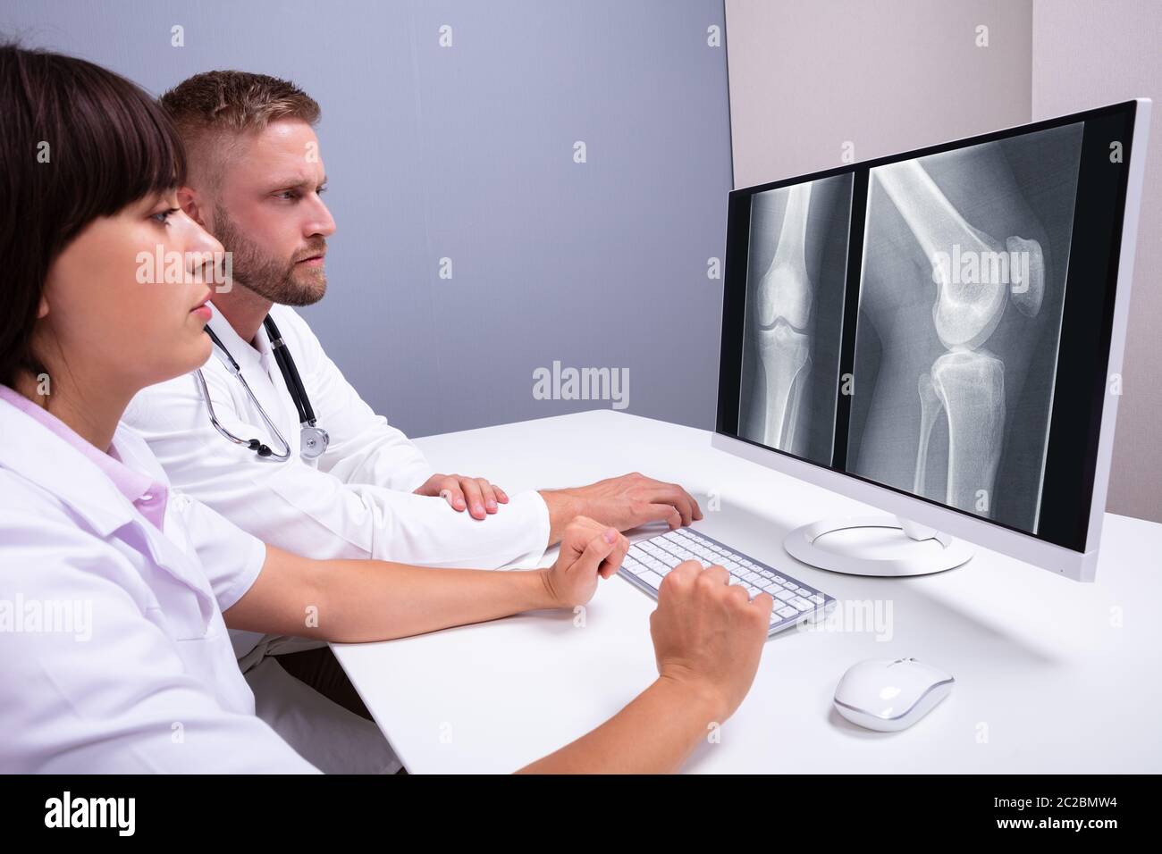 Doctors Examining Knee X-ray On Computer In Clinic Stock Photo