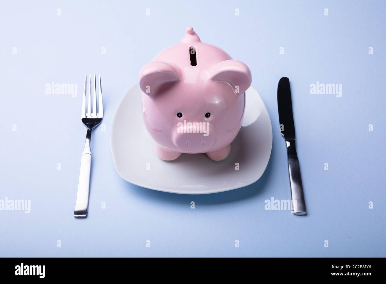 Elevated View Of Pink Piggy Bank On The White Plate With Fork And Knife Stock Photo