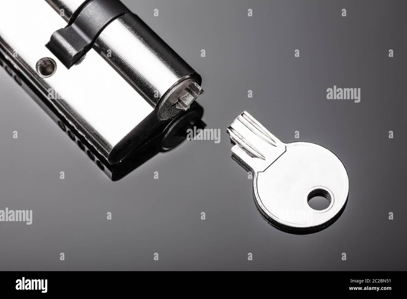 Close-up Of Pin Tumbler Of Cylinder Lock With Broken Key On Reflective Desk Stock Photo