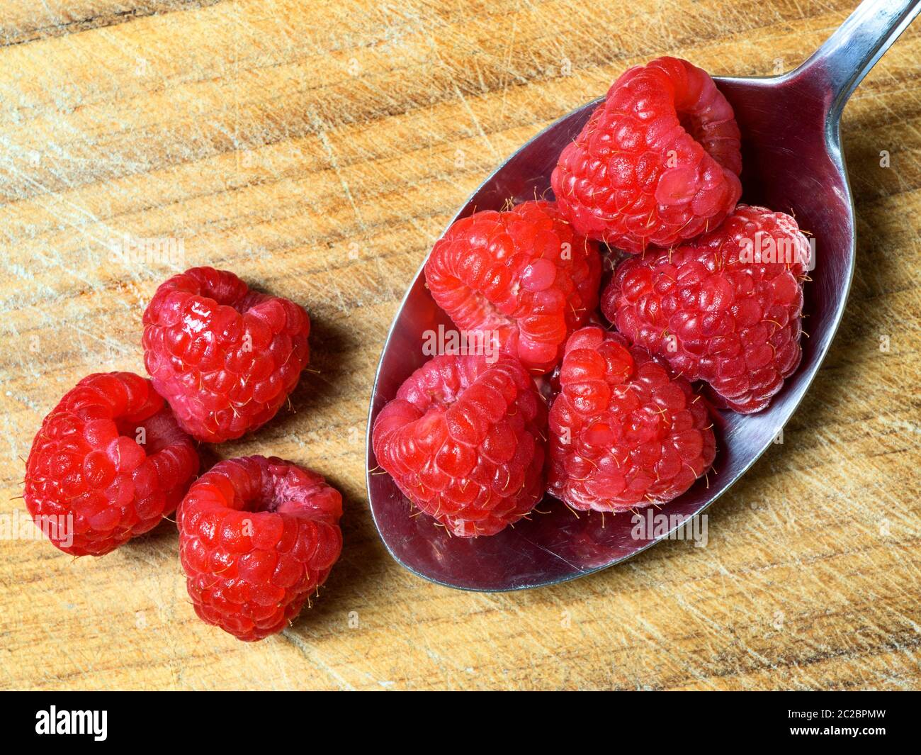 Five fresh raspberries in a stainless steel table spoon with three ...